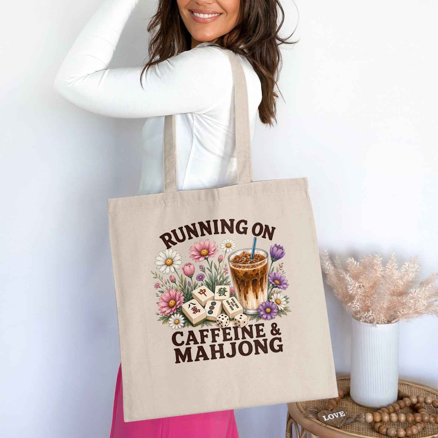 Tote bag with "Running on Caffeine & Mahjong" text, Iced coffee, mahjong tiles, flowers, and dice.
