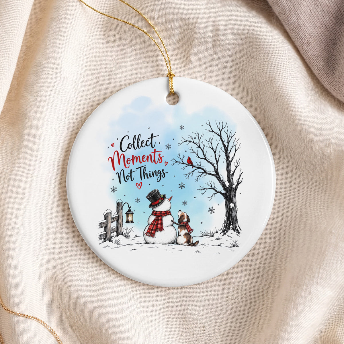Round white ceramic ornament featuring a winter scene with a snowman, dog, and the text Collect Moments Not Things.