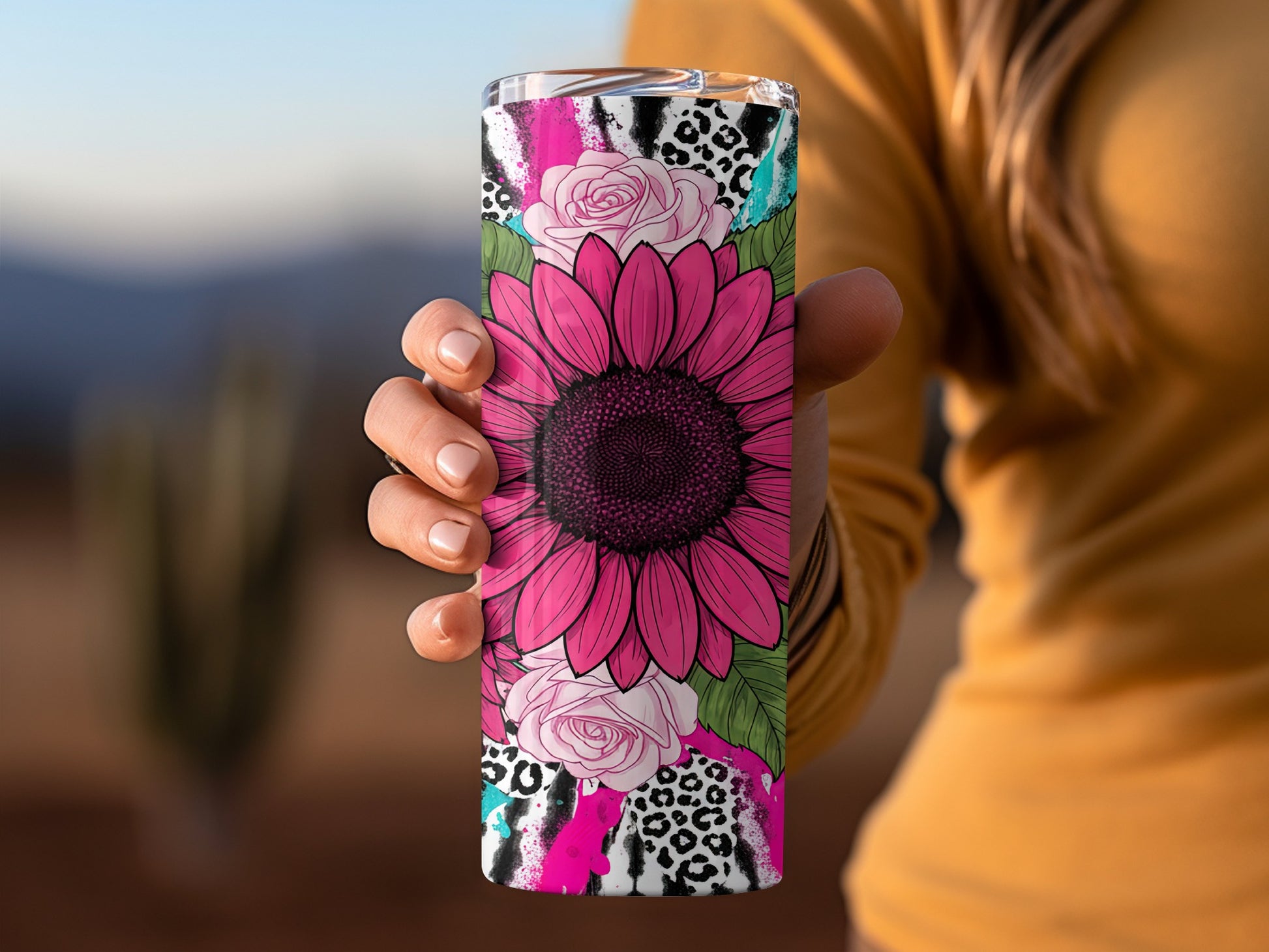 Sunflower and floral design on a tumbler held by a hand.