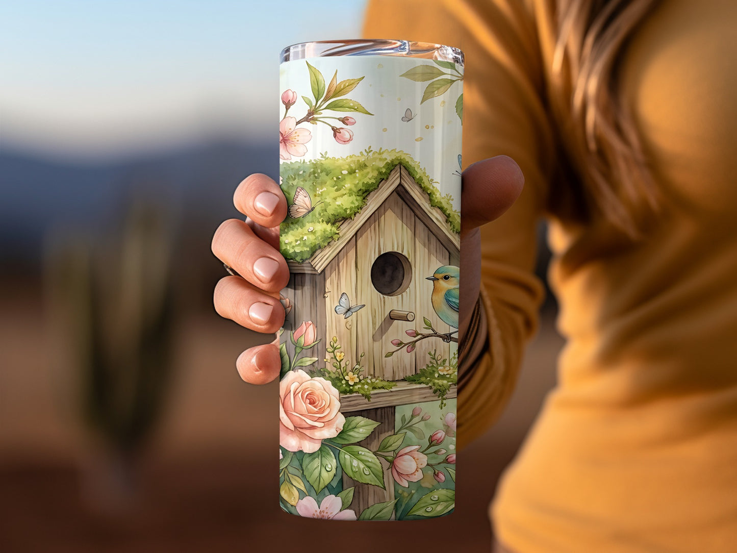 Birdhouse with flowers and butterflies, person holding a tumbler.