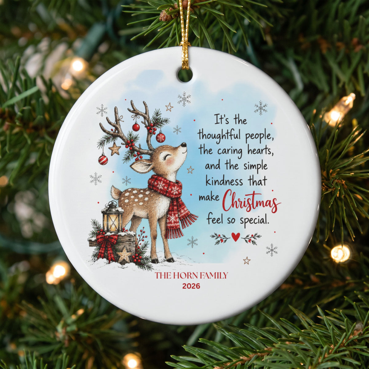 A round white ceramic Christmas ornament hanging on a tree, featuring a fawn illustration, holiday text, and customizable family name.