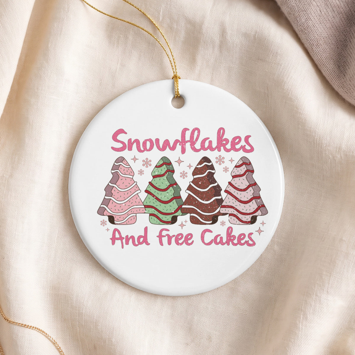 Round ornament with pink text "Snowflakes And free Cakes" and four decorated trees.