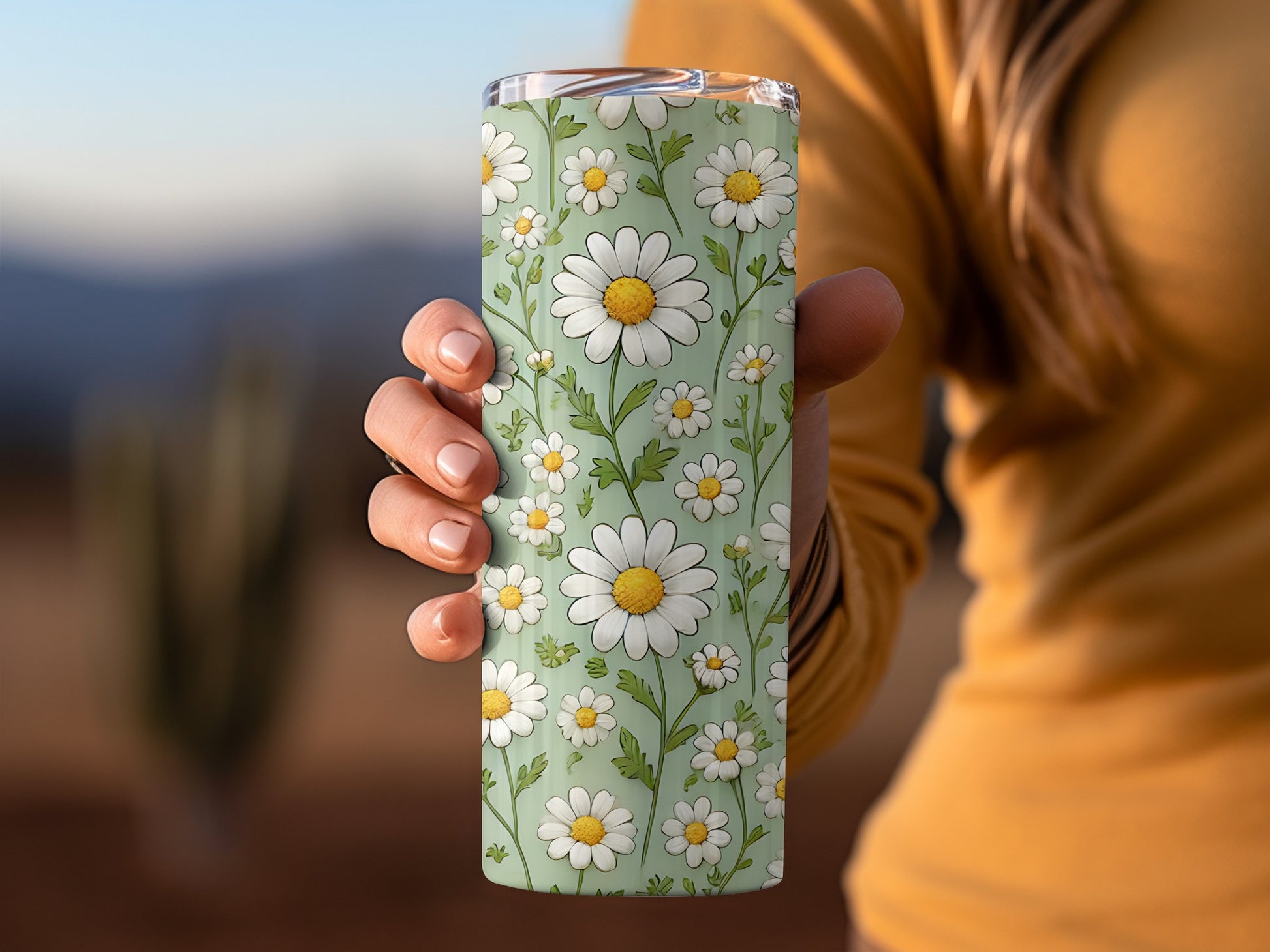 Green tumbler with daisy floral pattern held by a person.
