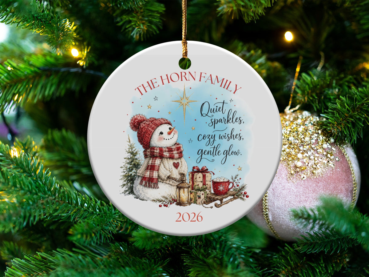 Round white ceramic Christmas ornament featuring a snowman, presents, and text that reads The Horn Family and 2026.