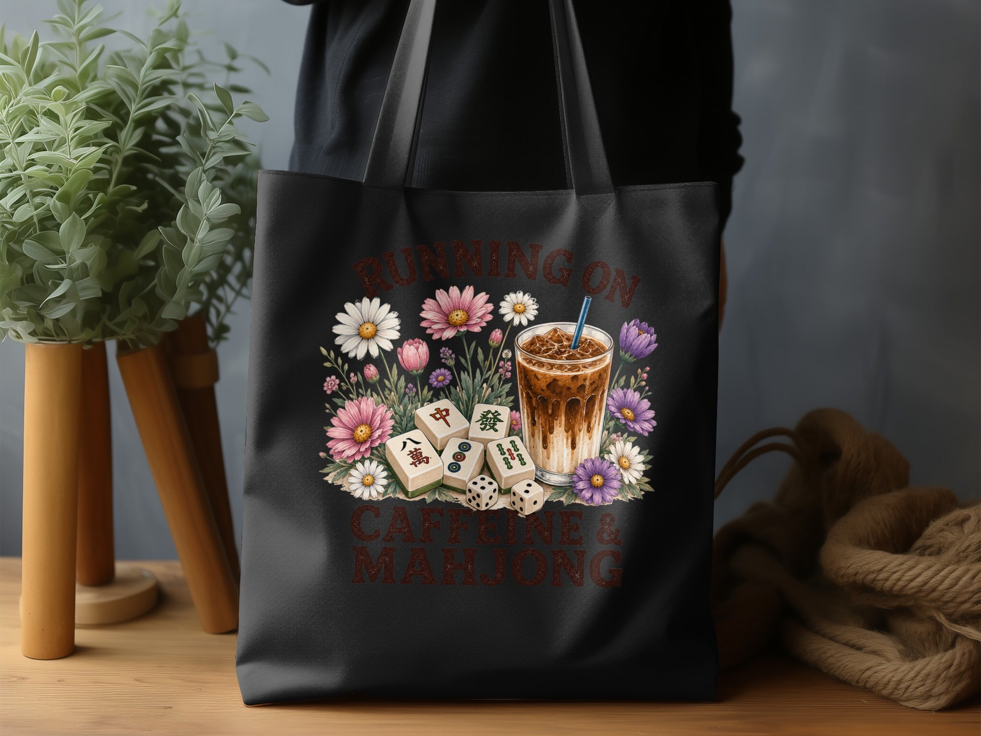 Black tote bag with "Running on Caffeine & Mahjong" and floral design.